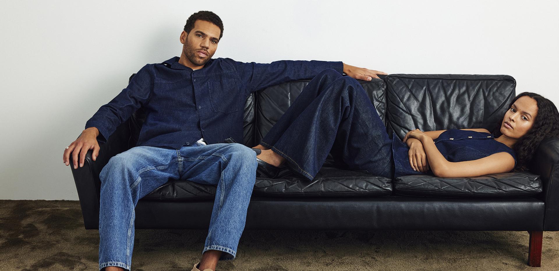 A man and a woman are lounging on a sofa, wearing denim outfits.